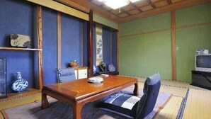 Ett traditionellt japanskt rum med tatamimattor på golvet, ett lågt träbord och en tv som står på ett stativ.