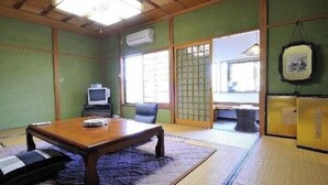 Ett traditionellt japanskt rum med tatamimattor på golvet, ett lågt bord, en tv och skjutdörrar som leder till ett annat rum.
