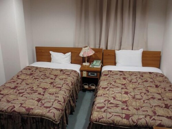 Habitación de hotel con dos camas individuales, cabecera de madera, mesita de noche con lámpara y teléfono.