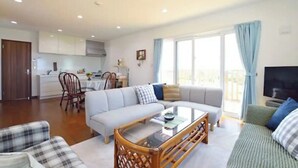 A modern living room with a sofa, a coffee table, and a television. There is a dining area with a table and chairs. - Ann Villa (Nakijin)