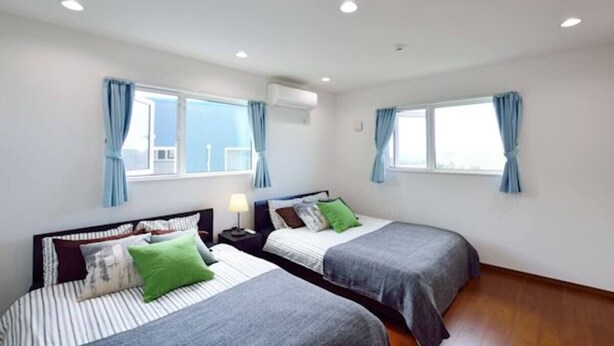 A bedroom with two beds, a window, and an air conditioning unit. - Ann Villa (Nakijin)