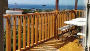 A balcony with a wooden railing, a white table, and a bench. - Ann Villa (Nakijin)