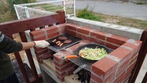 A brick grill with a person cooking hamburgers and a pan of food on a patio. - Ann Villa (Nakijin)