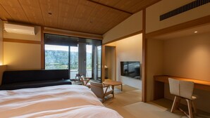 A modern hotel room with a large bed, a desk, a TV, and a balcony with a view of the forest. - Etchu Goi Hanao Onsen Yamaboushi (Takaoka)