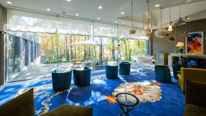 Una habitación amplia con un gran ventanal, alfombra azul con motivos florales y muebles modernos.
