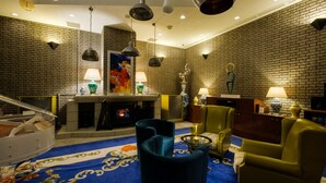 Un vestíbulo con pared de ladrillo, chimenea, sillones tapizados en azul y verde, y alfombra azul con estampado floral.