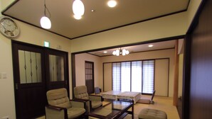 Una habitación tradicional japonesa con suelo de tatami, una mesa baja, dos sillones, un sofá y una puerta corredera.