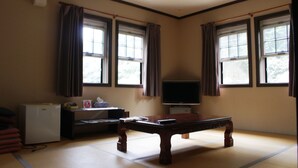 Una habitación con suelo de tatami, una mesa de madera, un televisor y un refrigerador.