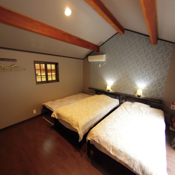 A room with two single beds, wooden beams on the ceiling, a window, and an air conditioning unit. - Tomonoyu Ryokan (Iwaki)