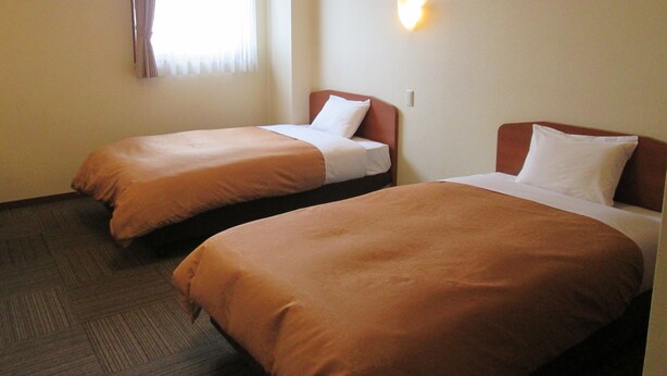 A hotel room with two single beds, a window with curtains, an air conditioning unit, and a wall-mounted light fixture. - Business Hotel Step In Haramachi (Minamisoma)