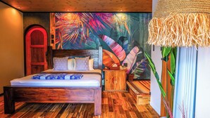 Un dormitorio con una cama de madera, una puerta roja, un mural de hojas tropicales y una lámpara de fibras naturales.