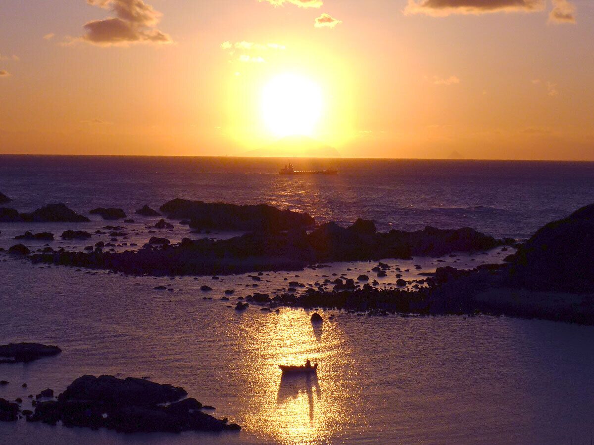 A sunset over a rocky coastline with a boat in the foreground.