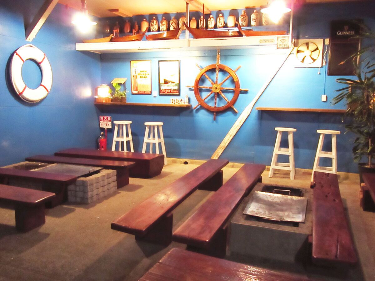 Um espaço de bar com bancos de madeira, um leme de navio e uma prateleira com garrafas.