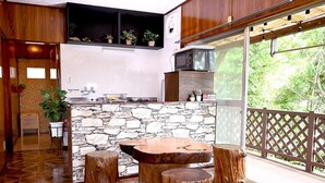 A modern kitchen with a stone backsplash, wooden stools, and a large window overlooking greenery. - Villa Ozawa (Shimoda)