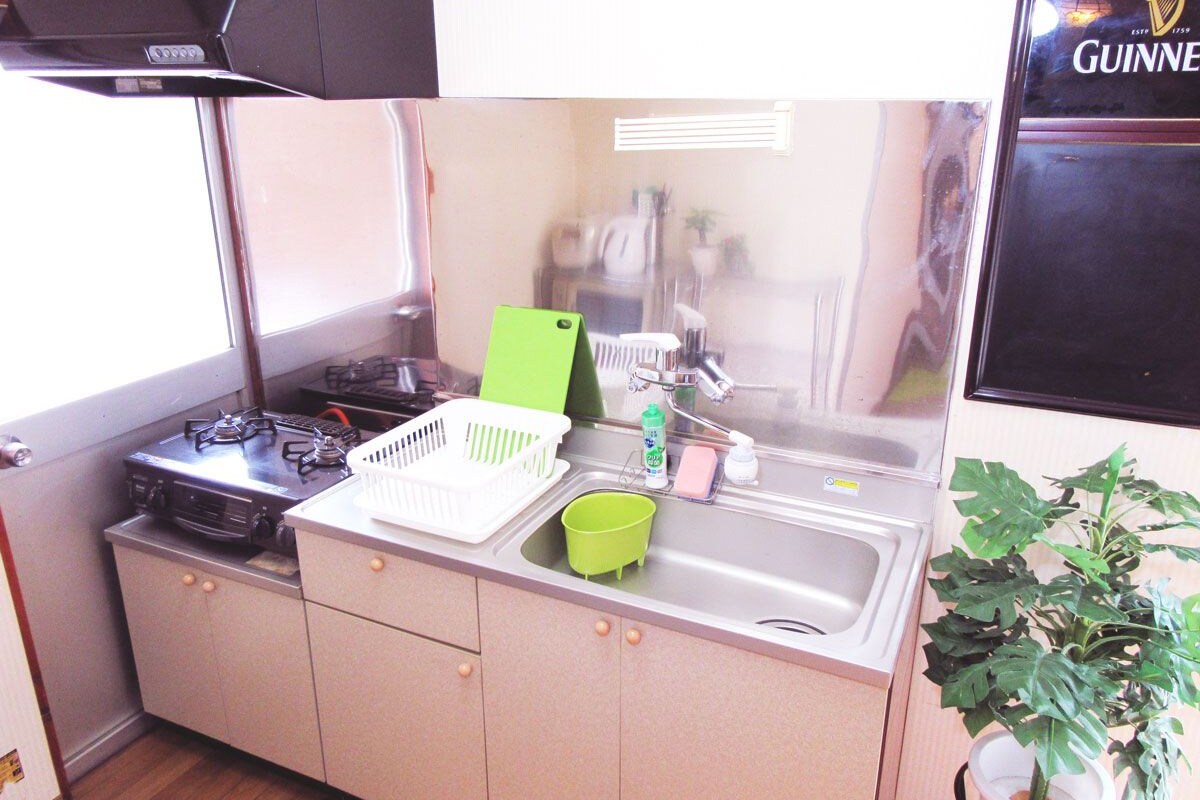 A compact kitchen with a gas stove, sink, and a green dish rack.