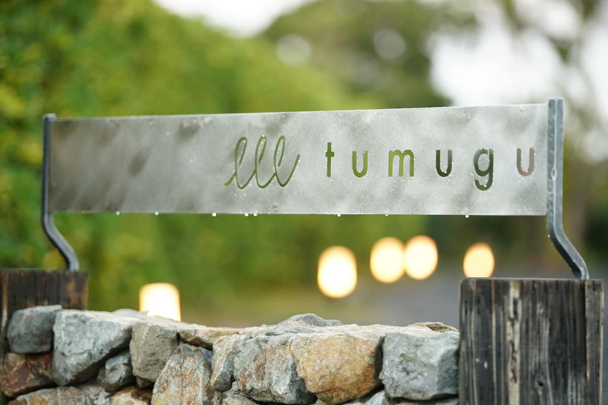 Une plaque métallique portant l’inscription « ell tumugu », fixée sur un poteau en bois.