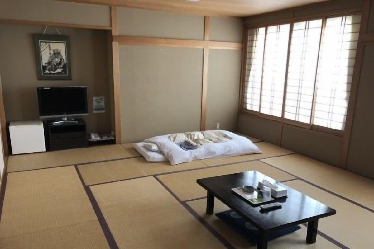 A tatami mat room with a low table, a TV, and a futon bed.