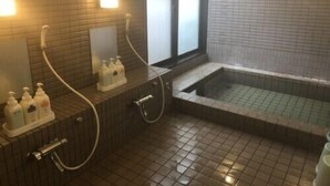 Um banheiro com piso ladrilhado, banheira, pia com dosadores de sabão e espelho.