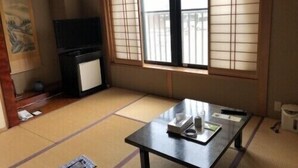 Quarto japonês tradicional com tatames, uma mesa baixa com bandeja, uma televisão e uma porta de correr com biombos shoji.