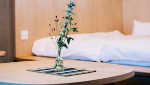 Ein Hotelzimmer mit einem Bett, einem Nachttisch mit Blumenvase und einem hölzernen Kopfteil.