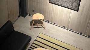 Ein modernes Zimmer mit einer schwarzen Couch, einem hölzernen Hocker, einem runden Tisch und einem großen, abstrakten Gemälde an der Wand.