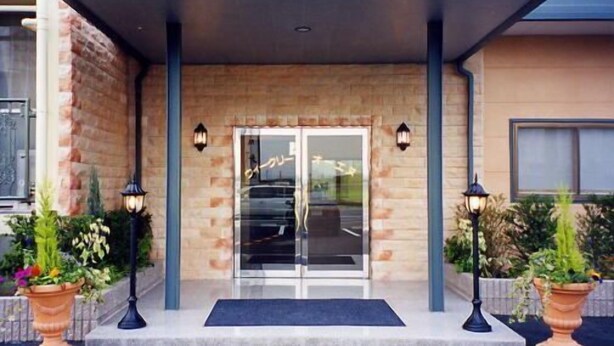 Entrada de hotel con puerta de vidrio, dos faroles laterales y felpudo.