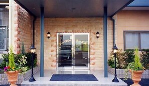 A hotel entrance with a glass door, two side lanterns, and a doormat. - Business Hotel Weekly Hotel Oenu (Iga)
