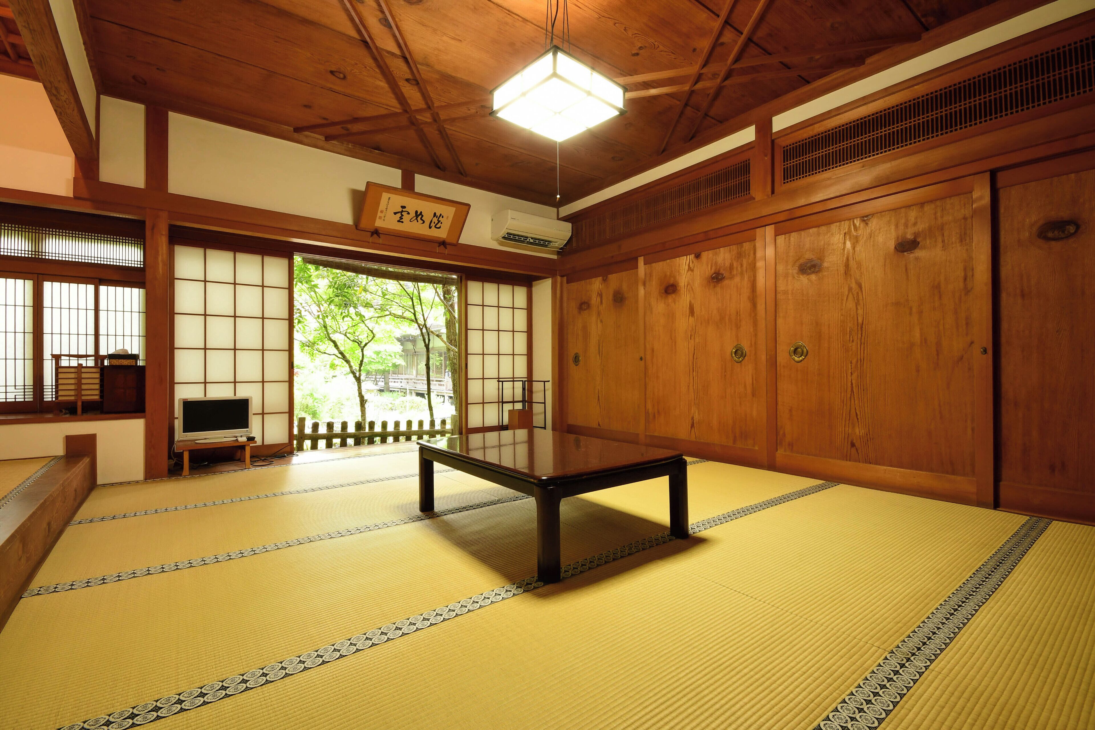 Una habitación con esteras de tatami, una mesa baja, puertas correderas de madera y un sistema de aire acondicionado de estilo japonés tradicional.