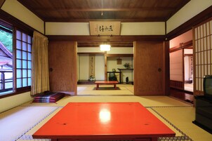 Una habitación japonesa tradicional con suelo de tatami, una mesa baja, puertas correderas y un televisor.