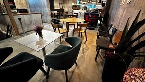 Et moderne restaurantinteriør med møbler i træ og metal, et centralt spisebord og et barområde.