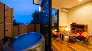 Ein Zimmer mit einer Steine-Badewanne, Holzboden, einem kleinen Tisch mit Kissen und Blick ins Freie.