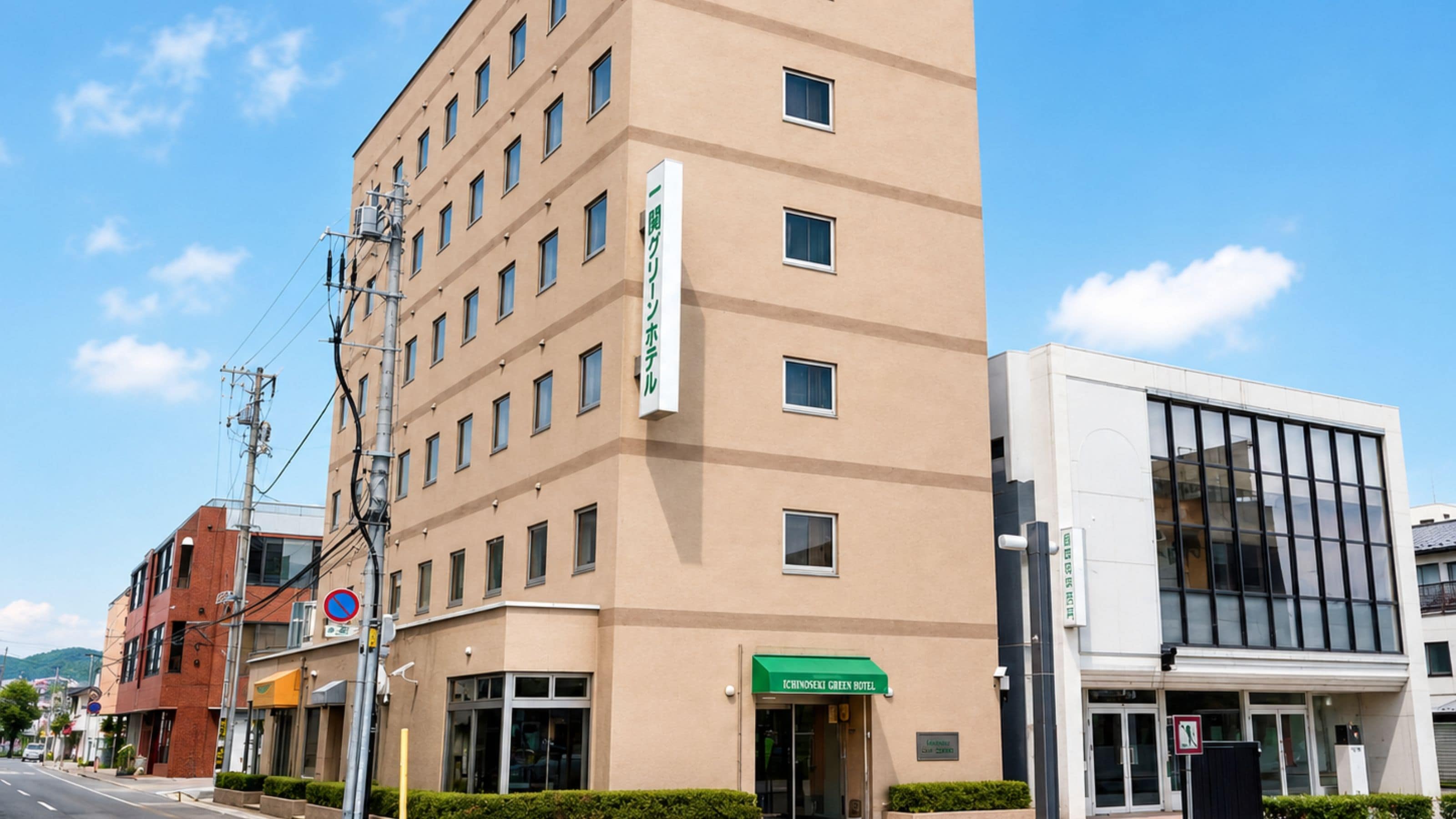 Un edificio de varios pisos con un letrero verde que indica un hotel. Se ve un cartel de no estacionamiento en la calle.
