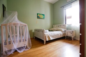 Une chambre à coucher avec un berceau, un lit, une table de chevet et une fenêtre avec des rideaux.