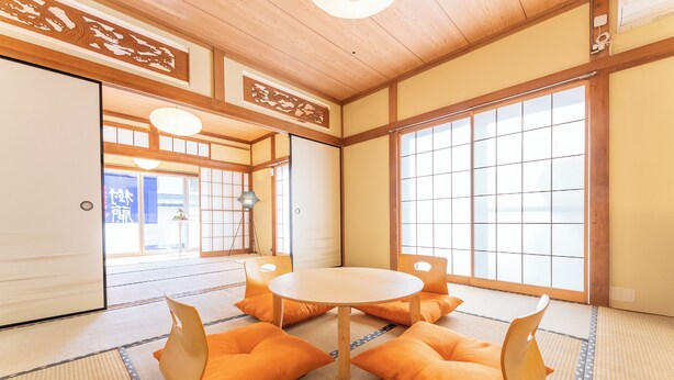 Une pièce de style japonais traditionnel, avec un sol recouvert de tatamis, une table ronde et des coussins orange.