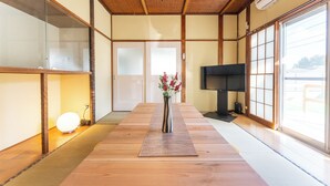 Une pièce de style japonais traditionnel, avec un sol recouvert de tatamis, un tapis de tatami au centre, un vase de fleurs, un téléviseur et des portes coulissantes.