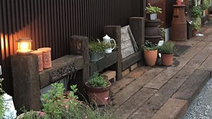 Un bâtiment à l’extérieur en bois foncé, avec un tableau encadré accroché au mur et plusieurs plantes en pot disposées le long de la façade.