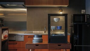 Une cuisine moderne avec des meubles en bois, une hotte en acier inoxydable, un meuble avec une porte en verre où sont rangés des bols, et un four à micro-ondes.