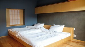Une chambre à coucher avec un lit en bois, du linge de lit blanc, une fenêtre à carreaux et un mur foncé.