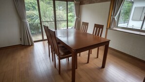 Une table à manger en bois, accompagnée de quatre chaises, se trouve dans une pièce dotée de grandes fenêtres.