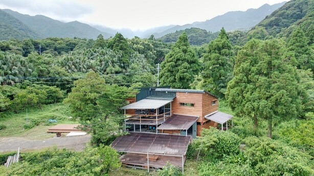 A wooden cabin with a metal roof, surrounded by dense forest and mountains. - Nagatatime (Yakushima)