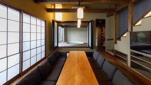 Una habitación tradicional japonesa con asientos de estera de tatami, una mesa de madera y vistas a un jardín a través de un puertas correderas.