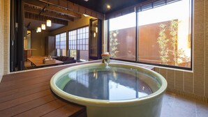 Jacuzzi en una habitación con ventanas amplias, piso de madera y vistas a plantas de bambú al exterior.