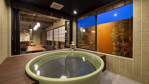 Un onsen japonés tradicional con una terraza de madera, una tina grande para remojar, puertas correderas y vistas al cielo nocturno.