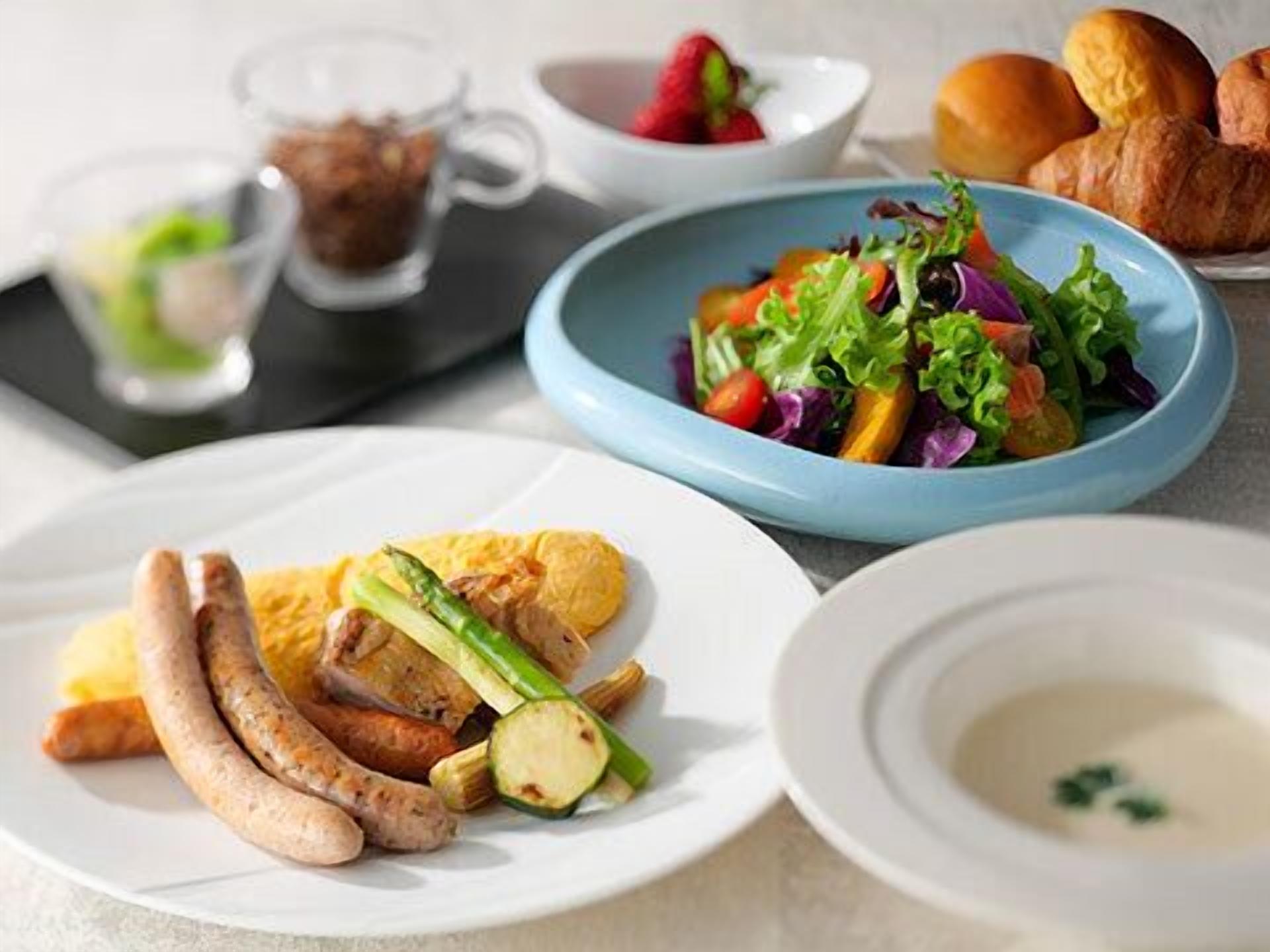 A dining table with plates of food, including sausages, vegetables, and a salad.