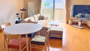 Un salon moderne comprenant un canapé, une table à manger avec des chaises, un téléviseur et un balcon avec des rideaux.