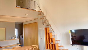 Un intérieur moderne avec un escalier en bois, un coin repas comprenant une table et des chaises, et un téléviseur fixé au mur.