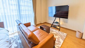 Un salon moderne avec un canapé en cuir, un téléviseur à écran plat posé sur un meuble, une grande fenêtre ornée de rideaux légers et un tapis à motifs.