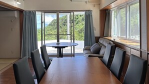 A room with a wooden table and chairs, a sofa, and a large window with curtains. - Sunrise Vista Nanjo (Nanjo)