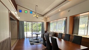 A spacious room with a long wooden table, several chairs, a sofa, and large windows providing natural light. - Sunrise Vista Nanjo (Nanjo)