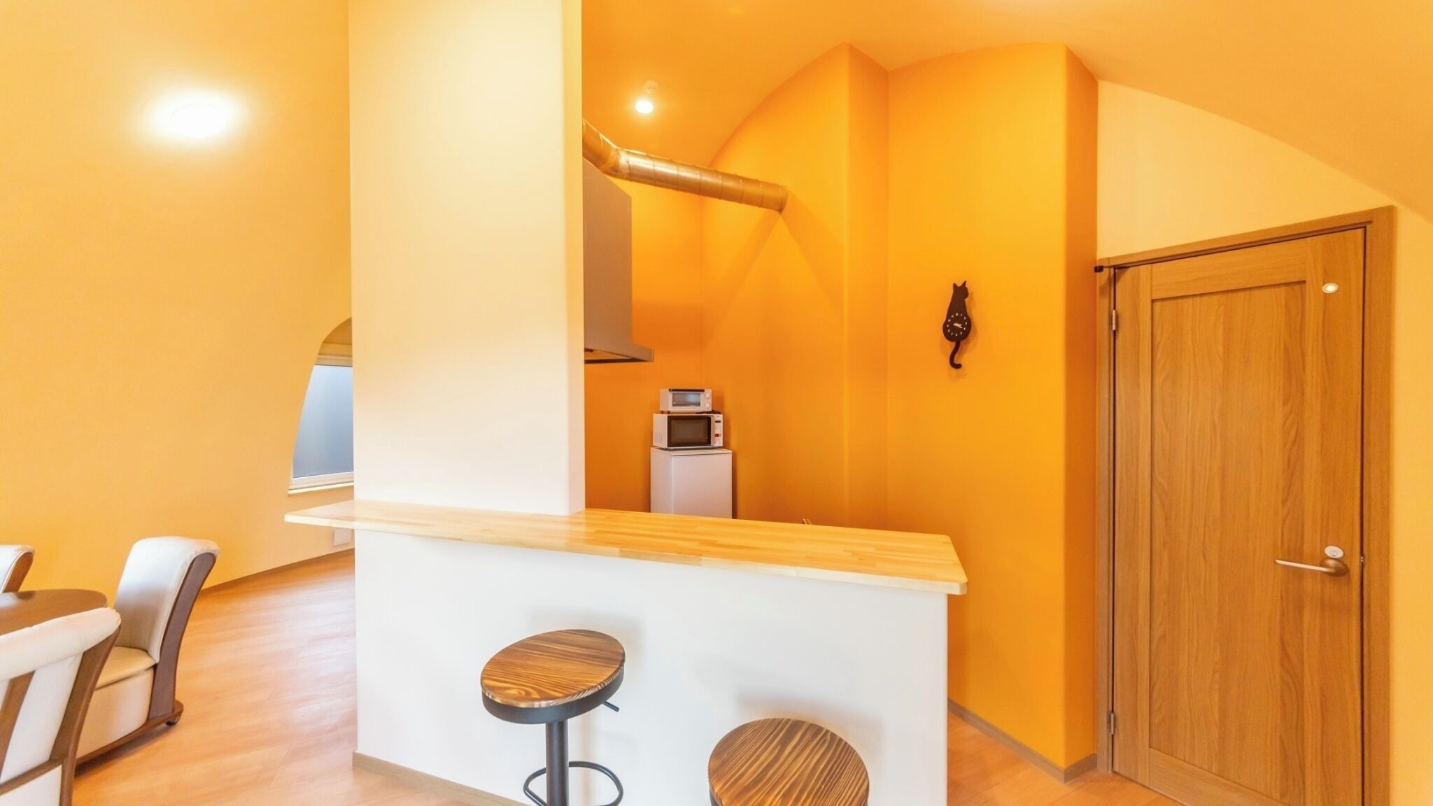 A compact kitchen with a microwave, a clock, and a wooden door.